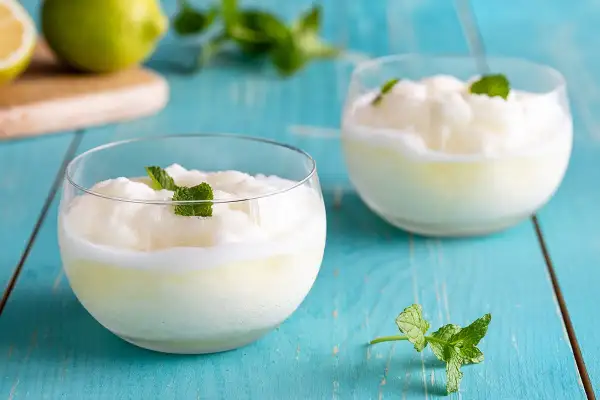 Due bicchieri di sorbetto al limone, guarniti con menta fresca, su un tavolo di legno blu.
