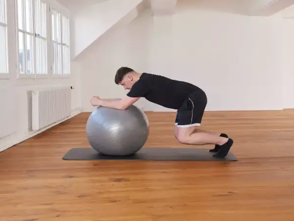 Un homme effectue un exercice de gainage avec un ballon de gym, en appui sur ses avant-bras et ses genoux.
