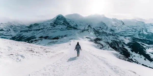 Une personne marche sur un sentier enneigé, dominant des montagnes majestueuses. Un paysage hivernal à couper le souffle, typique d'Interlaken, Suisse.