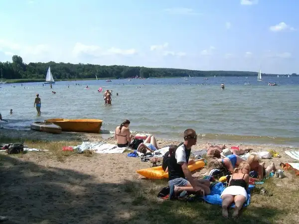 Ludzie odpoczywają na plaży, pływają i żeglują. To typowe **Boszkowo atrakcje** w słoneczny dzień.
