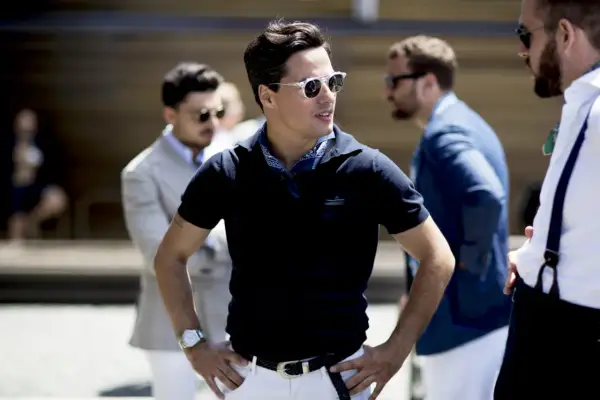 Ein Mann in einem dunkelblauen Poloshirt mit weißem Gürtel und weißer Hose, dazu ein blaues Halstuch. Ein stilvolles Outfit für Herren.
