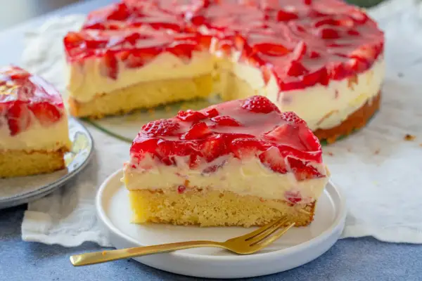 Ein saftiger Erdbeer Schmand Kuchen mit frischen Erdbeeren und glänzendem Tortenguss. Ein Stück auf einem Teller mit Gabel.