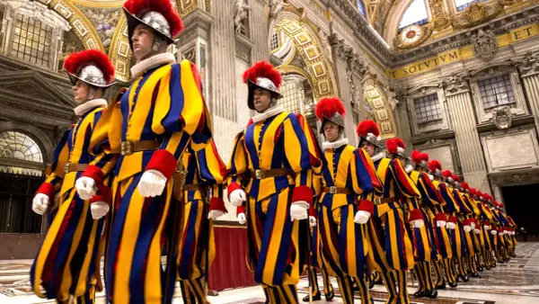 Guardia suiza del Vaticano desfila en formación, con sus icónicos uniformes a rayas amarillas, azules y rojas, y penachos rojos.