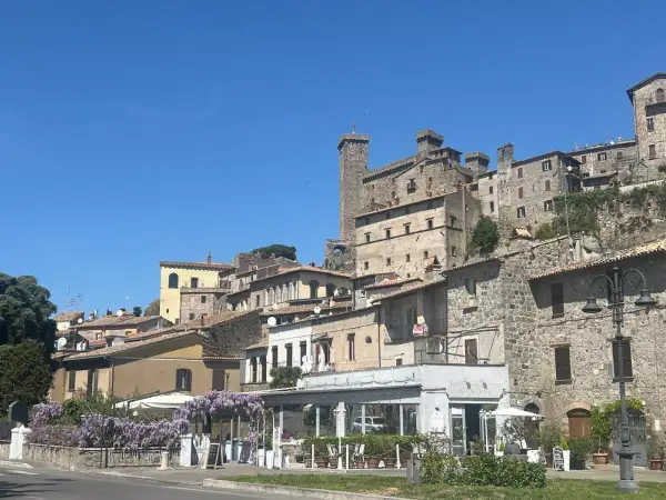 Borgo medievale sul lago di Bolsena, cosa vedere: un castello imponente, case in pietra e un ristorante fiorito.