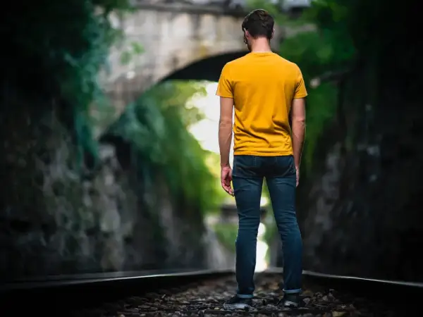 Man op spoor, omringd door groen. Een metafoor voor het navigeren door het leven met hsp, waar elke stap bewust gezet moet worden.