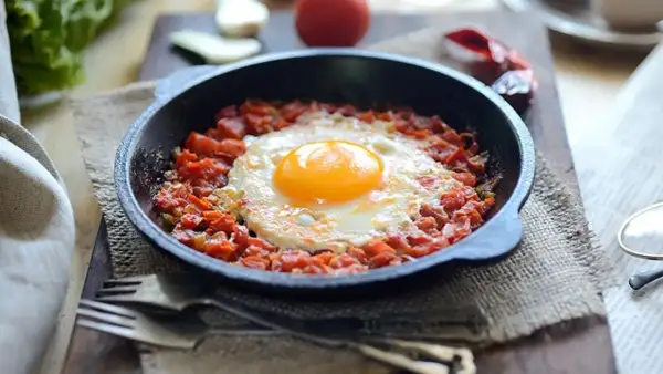 Un huevo frito sobre una cama de tomate picado en cazuelitas de aperitivo, listo para disfrutar.