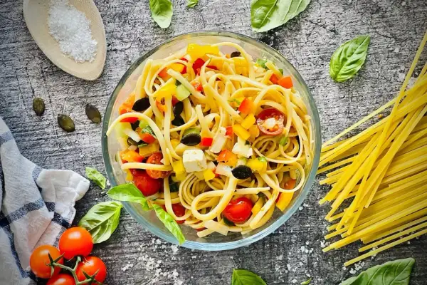 Frischer Spaghetti Salat mit bunten Paprika-, Tomaten- und Olivenstücken, garniert mit Basilikum.
