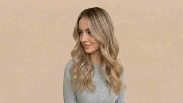 Kobieta z falowanymi, piaskowymi blond włosami, które delikatnie opadają na ramiona.