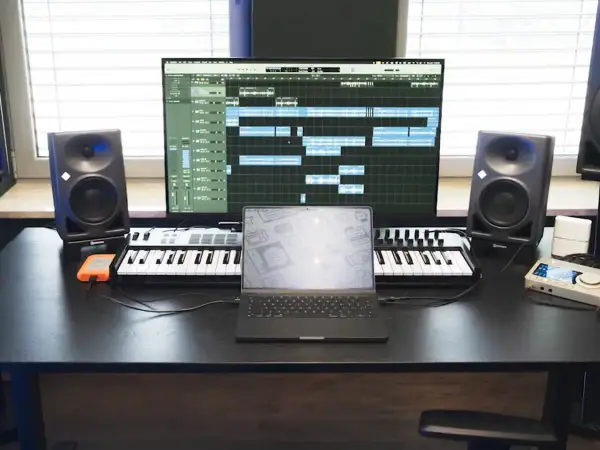 Studio do nagrywania muzyki: monitory studyjne, klawiatury MIDI, laptop i ekran z sekwencerem.