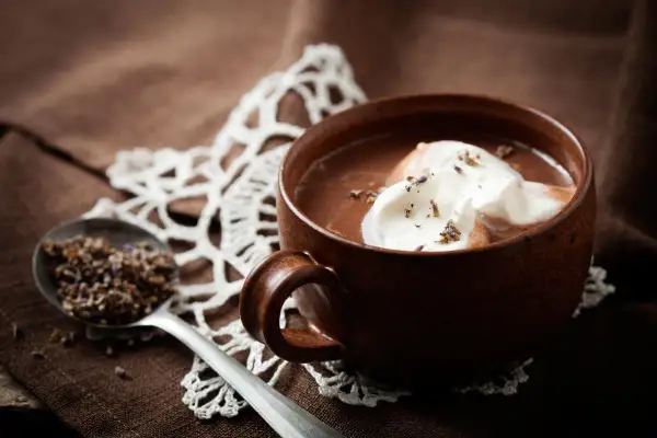 Una tazza di cioccolata calda senza cacao, con panna montata e lavanda. Un cucchiaio contiene lavanda secca.