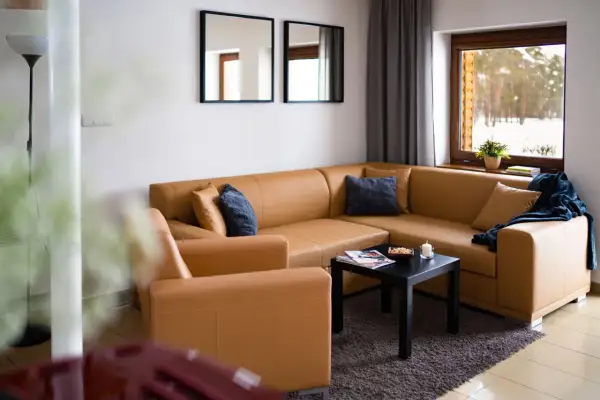 Przytulny salon z brązową kanapą i fotelem, z widokiem na zimowy las. Idealne miejsce na odpoczynek, jak w **starej wsi**.