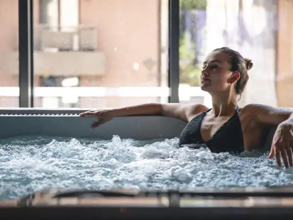 Kobieta relaksuje się w jacuzzi, zastanawiając się, czy jacuzzi odchudza. Woda bąbelkuje wokół niej.