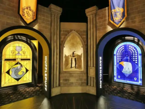 Wystawa Harry Potter: witraże Hufflepuff i Ravenclaw, a w centrum figura z kapeluszem.