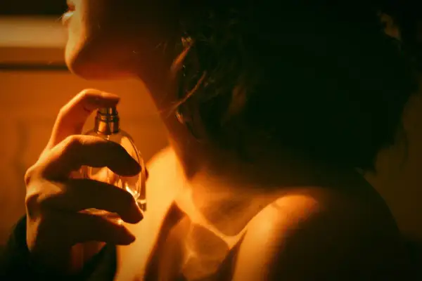 Kobieta aplikuje perfumy. Czy to zapach gourmand? Ciepłe światło podkreśla jej szyję i ramię.