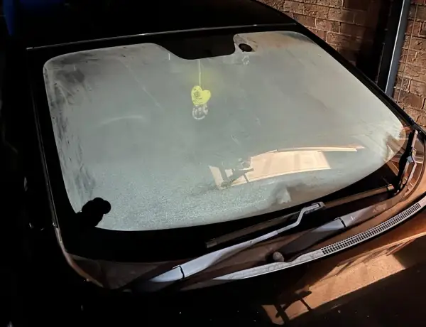 En frostig vindruta på en bil. En gul hjärtformad doftgran hänger från backspegeln.
