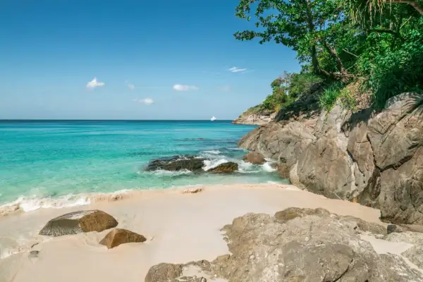 Piękne plaże Phuket z turkusową wodą, piaszczystym brzegiem i skalistym wybrzeżem. Na horyzoncie biała łódź.