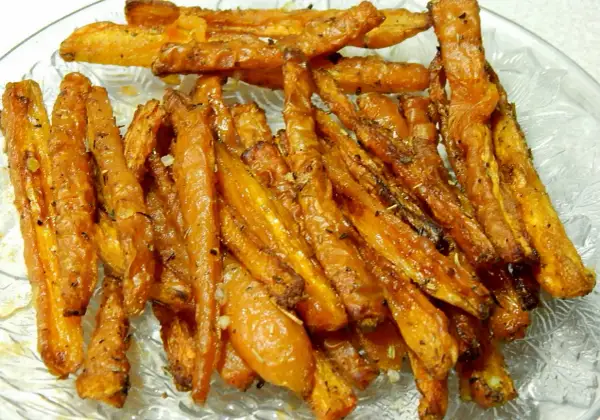Chrupiące, pieczone frytki z marchewki, przyprawione ziołami i czosnkiem, ułożone na szklanej tacy.