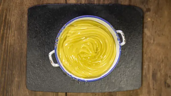 Una ciotola di cremosa crema pasticcera vegana, con un vortice lucido al centro, pronta per farcire dolci.