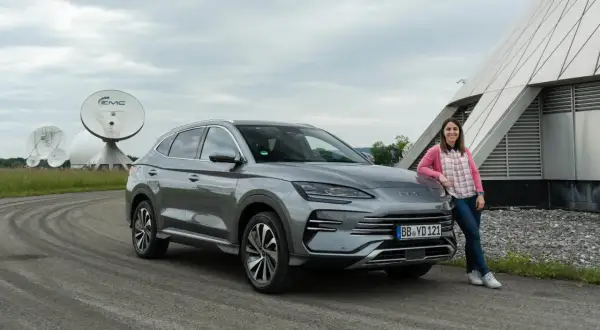 Mujer sonríe junto a un BYD Seal U, disfrutando del dm-i comfort en un día nublado, con antenas parabólicas de fondo.