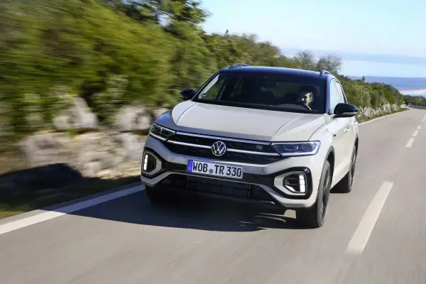 Jasnoszary Volkswagen T-Roc jedzie po krętej drodze. Nawet przy potencjalnych volkswagen t-roc usterki, auto prezentuje się dynamicznie.