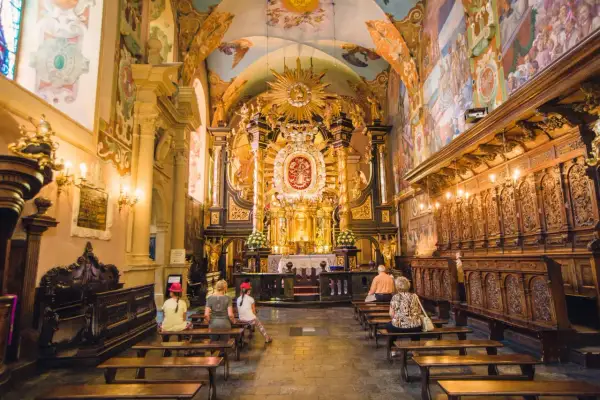Wnętrze sanktuarium pasyjno-maryjnego w Kalwarii Zebrzydowskiej. Złoty ołtarz, malowidła na ścianach i sklepieniu, wierni na ławkach.