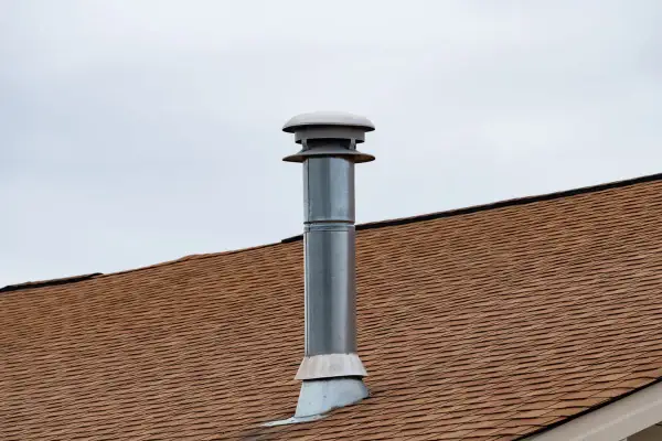 Cheminée sans tubage sur un toit brun sous un ciel couvert. La cheminée est en métal avec un chapeau ventilé.