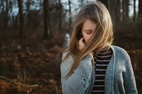 Smutna dziewczynka w lesie, jej włosy zasłaniają twarz. Czuła, że antydepresanty zniszczyły jej życie, odbierając radość.