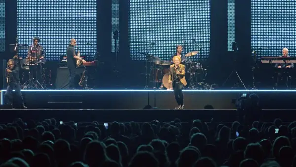 Ein Musiker mit goldenem Sakko singt auf der Bühne, umgeben von seiner Band. Ein Konzert von Simply Red in Stuttgart.