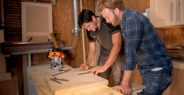 Carpinteros trabajan con madera calabo en un taller. Uno marca una pieza de madera mientras el otro observa.