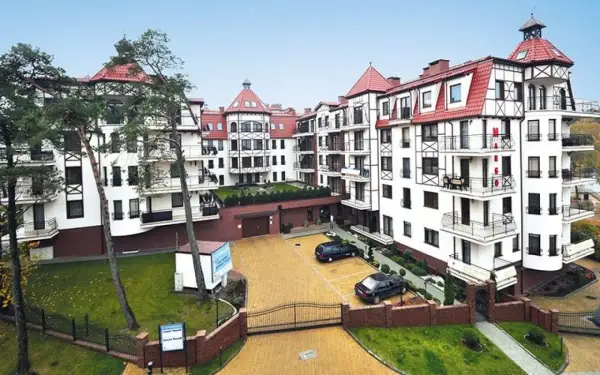 Elegancki budynek w stylu alpejskim, przypominający Continental Hotel Krynica, z białymi fasadami, czerwonymi dachami i drewnianymi elementami.