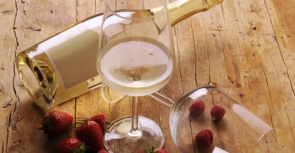 Butelka i kieliszek pełne musującego płynu, obok truskawki i maliny. To jest prosecco, idealne na letnie popołudnie.