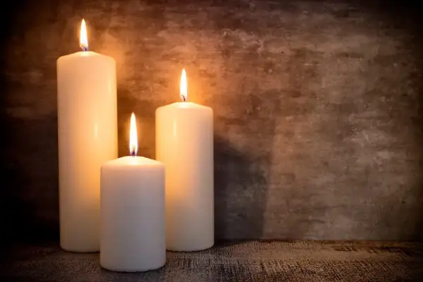 Tre candele di cera bianca illuminate, con fiamme danzanti, su uno sfondo scuro. Un'atmosfera intima, perfetta per riflettere su dove si buttano le candele di cera.