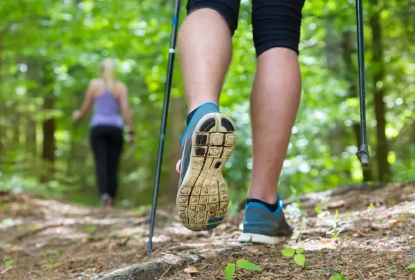 Osoba w bucikach na kijki nordic walking stawia krok na leśnej ścieżce.