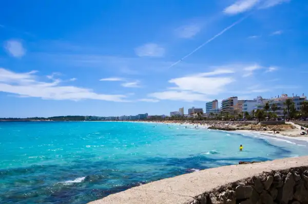 En livlig Cala Millor Beach med turkost vatten, solbadande människor och hotell längs kusten under en klarblå himmel.