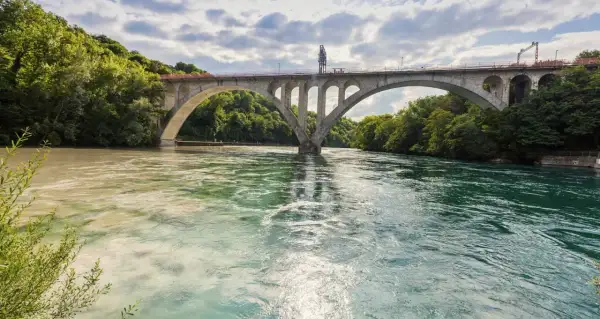 Ponte ad arco su fiume con acque di colori diversi, dove si intravedono segnali navigazione fluviale.