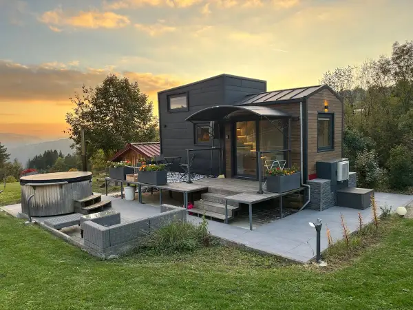 Tiny house dans le Jura, avec jacuzzi et mobilier extérieur, au coucher du soleil.