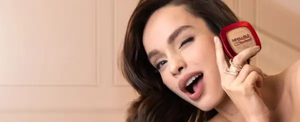 Uśmiechnięta kobieta prezentuje puder L'Oréal Infallible 24H Fresh Wear.