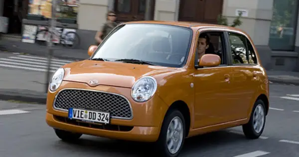 Pomarańczowy Daihatsu Trevis z kierowcą za kierownicą jedzie ulicą.