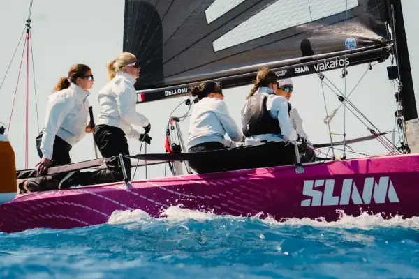 Equipaggio femminile su barca a vela rosa, con la vela nera e il logo SLAM. Le veliste si preparano per la regata RS 21.