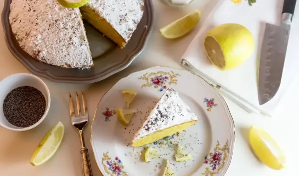 Una fetta di torta al limone leggerissima, spolverata di zucchero a velo e semi di papavero, guarnita con spicchi di limone fresco.
