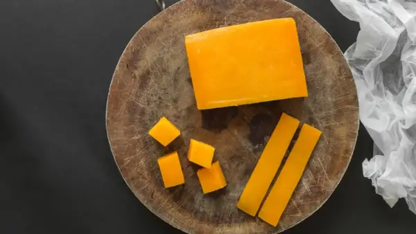 Un bloque de queso color naranja, cortado en cubos y bastones, sobre una tabla de madera.