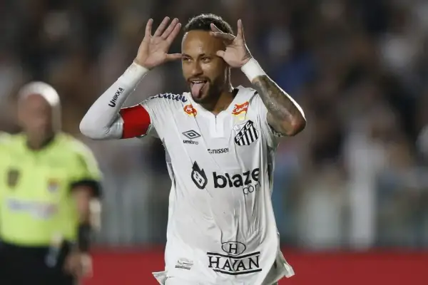 Neymar w białej koszulce Santos z czerwonymi opaskami na ramionach, pokazuje język i robi śmieszne miny.