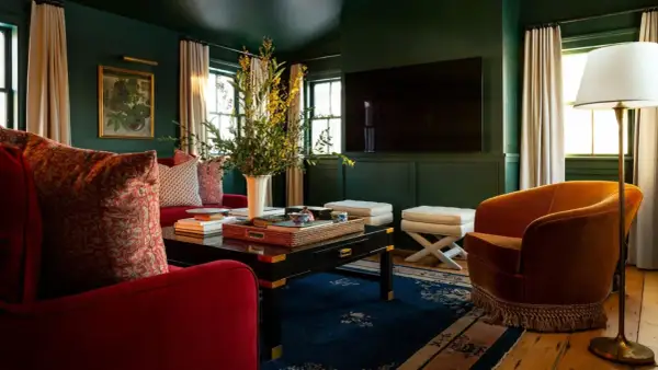 A rich, jewel-toned living room with plush red sofas, an orange velvet armchair, and a dark coffee table, showcasing timeless interior design.