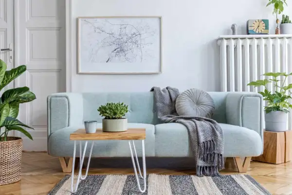 A light blue couch with a throw blanket and pillow. A small wooden table with a plant sits on the couch. This image shows how to clean a couch.