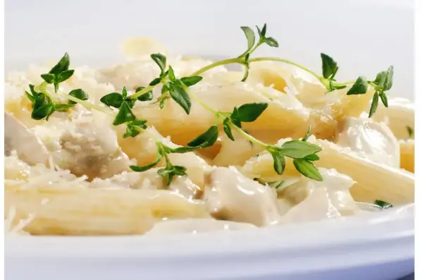 Penne z kurczakiem w kremowym sosie jogurtowym, posypane parmezanem i udekorowane gałązkami tymianku.