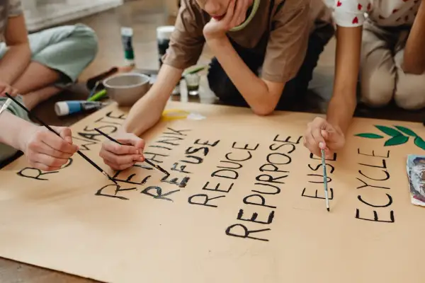 Niños pintan un cartel sobre la **competencia ciudadana LOMCE** y el reciclaje: "RETHINK, REFUSE, REDUCE, REPURPOSE, REUSE, RECYCLE".