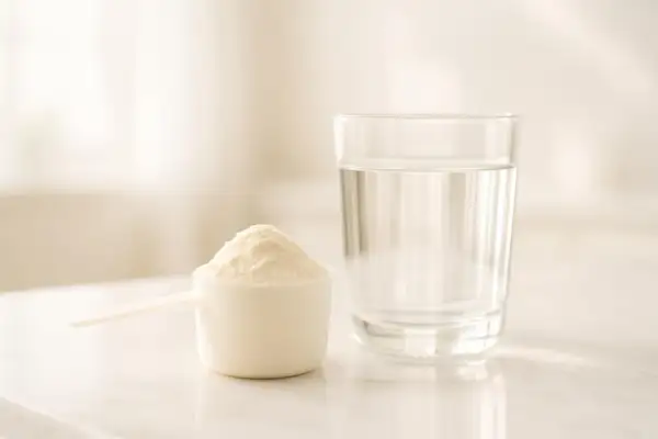 Un misurino di polvere bianca accanto a un bicchiere d'acqua, una sana alternativa alle proteine in polvere.