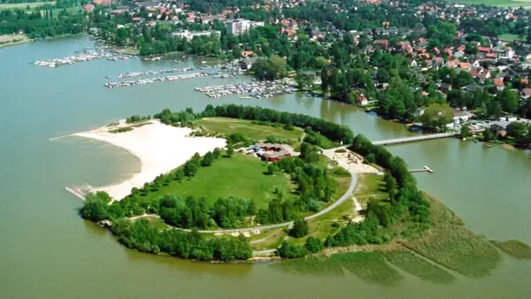 Grüne Insel mit Sandstrand und Gebäuden im Steinhuder Meer, umgeben von einem Yachthafen und einer Ortschaft.