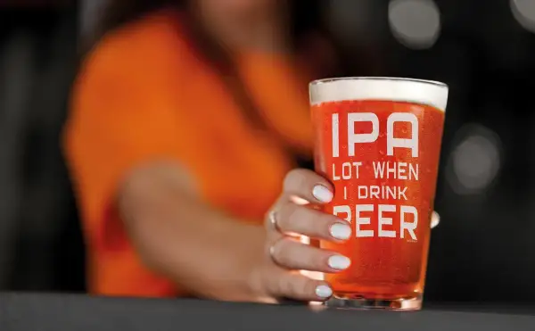 Un bicchiere di IPA con la scritta "IPA LOT WHEN I DRINK BEER" tenuto da una mano con unghie bianche.