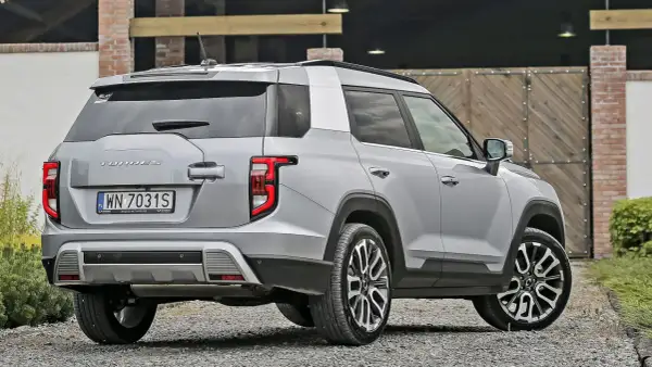 Srebrny SsangYong Torres z polskimi tablicami rejestracyjnymi WN 7031S stoi na żwirowej drodze przed drewnianą bramą.